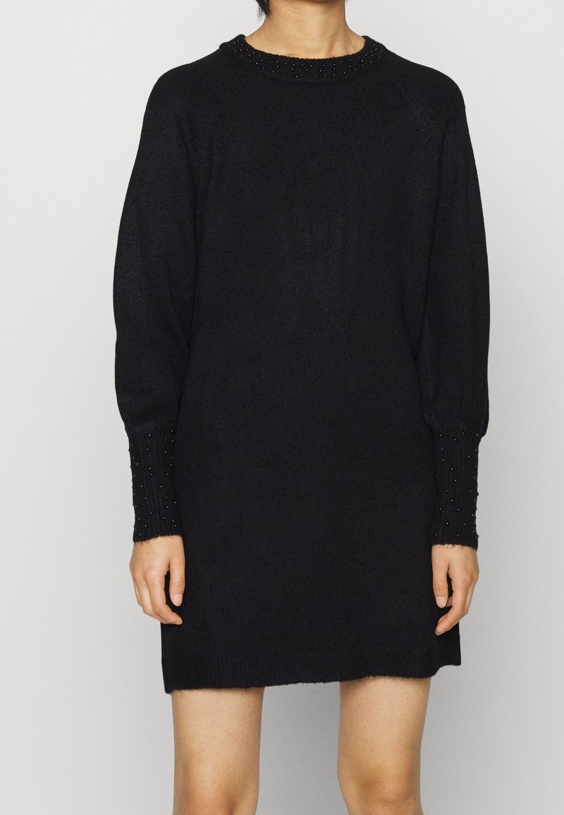 Svart stickad klänning med avslappnad passform, med en ribbad hals och manschetter prydda med små svarta pärlor. Mjuk textur och längd över knäna.