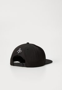Svart snapback caps med flat brem og justerbar stropp bak. Brodert logo detalj i hvitt på baksiden. Glatt stofftekstur.