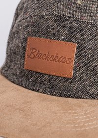 Cap featuring a dark textured fabric with multicolored flecks, tan suede brim, and a brown leather patch labeled "Blackskies."