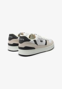 Sneakers Lacoste con pannelli bianchi, beige e neri. Materiali in suede e pelle con una superficie testurizzata. Presentano una soletta imbottita e il logo.