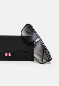 Ochelari de soare aviator negri cu lentile gri degradate, având un cadru solid și detaliu cu logo. Însoțiți de o carcasă elegantă neagră.