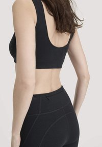 Vrouw in een zwarte sportbeha en hoge zwarte leggings, gezien vanaf de achterkant met los bruin haar.