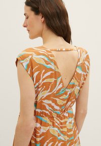 Orangenes Kleid mit einem v-förmigen Rücken, das ein florales Muster in Blau, Gelb und Weiß aufweist, aus leichtem Stoff mit kurzen Ärmeln.