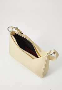Gul kunstskinn crossbody-veske med glidelås i sølv, en vinklet design og svart interiør med røde detaljer. Justerbar stropp følger med.