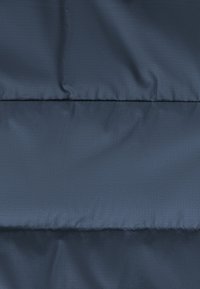 Marineblaue, gepolsterte Stoff mit glatter Textur, ausgestattet mit horizontalen Nähten und einem subtilen Rautenmuster. Strapazierfähiges, wasserabweisendes Material.