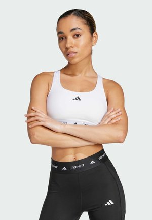 Sutien sport alb cu logo negru, asociat cu colanți negri cu un talie branduită. Textură netedă, design mulat pentru îmbrăcăminte sport.
