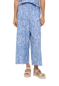 Niebieskie spodnie z szerokimi nogawkami w kwiatowy wzór z białymi zdobieniami, wykonane z lekkiego materiału. Zestawione z beżowymi sandałami na platformie.