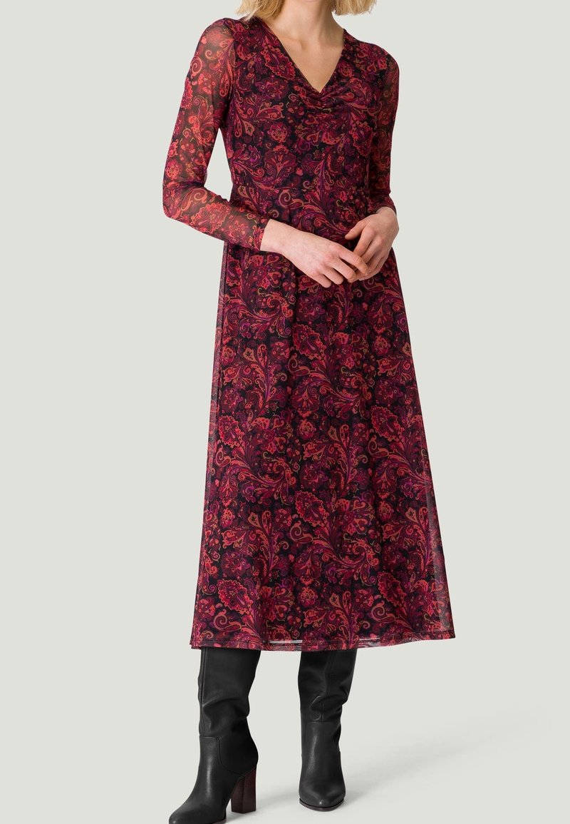 Lång bordeauxfärgad klänning med blommönster; genomskinliga långa ärmar; V-ringning; kombinerad med knähöga svarta stövlar; flödande A-linjeformad silhuett.