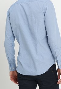 Lichtblauw button-up shirt met een patroon van kleine stippen, lange mouwen en een afgeronde onderkant, gemaakt van een gladde stof.
