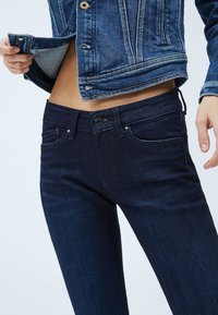 Mörkblå denimjeans med slim fit, med knappstängning, framfickor och subtila sömmar. Matchade med en blå denimjacka.
