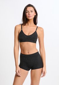 Sujeción deportiva negra de elastano con escote redondeado y tirantes finos ajustables, combinada con unos pantalones cortos de talle alto a juego. Textura brillante.