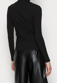 Zwarte geribbelde coltrui met lange mouwen, aansluitend design, zachte textuur. Gecombineerd met zwarte leren wijde broek. Soepele en strakke afwerking.
