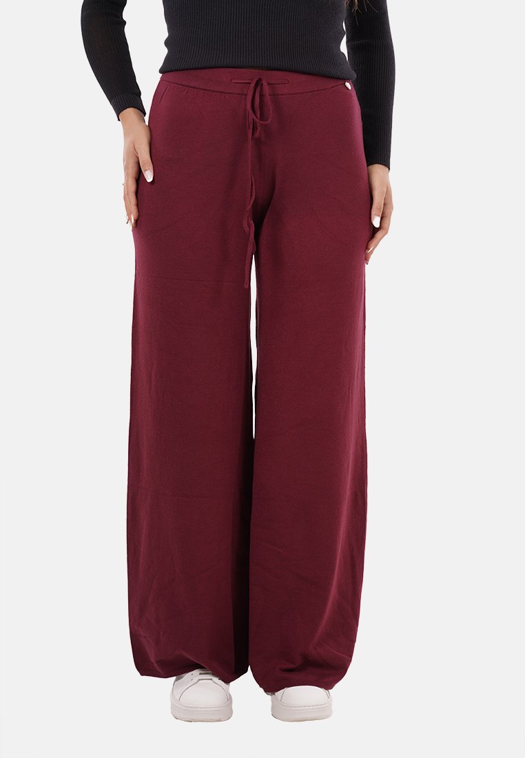 Pantaloni larghi bordeaux realizzati in morbido cotone, con vita regolabile e tasche frontali. Sneakers bianche indossate sotto.
