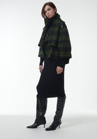 Groen en zwart geruite jas met een gedrapeerd ontwerp; ribbel zwart jurkje en kniehoge zwarte leren laarzen met puntige neuzen.