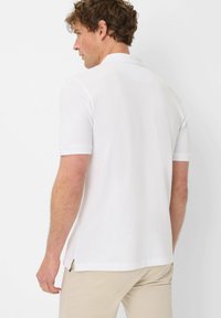 Polo shirt bianco a maniche corte con colletto a maglia piatta, spacco laterale e texture liscia, visto dal retro.