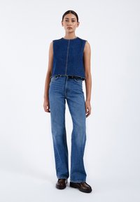 Top sin mangas de denim azul con corte recto y dobladillo deshilachado, combinado con jeans azules de cintura alta y zapatos de plataforma marrón oscuro.