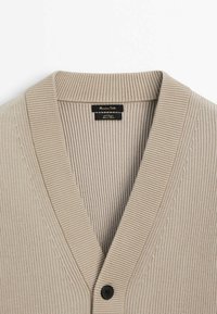 Beige geripptes Cardigan mit V-Ausschnitt, ausgestattet mit einem einzelnen schwarzen Knopf und einem strukturierten Stoff. Das Etikett zeigt "Massimo Dutti."