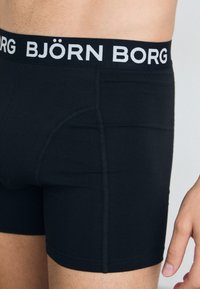 Boxer-briefs noirs avec une taille élastique blanche arborant "BJÖRN BORG." Dotés d'un ajustement près du corps, d'une texture lisse et de coutures renforcées.