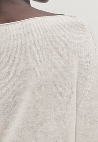 Pull tricoté beige clair avec une coupe ample et un col bateau. Présente un motif de point texturé, des coutures apparentes et un tissu doux.