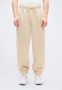 Beige sweatpants with a drawstring waistband, tapered cuffs, and white side stripes. Made of soft fabric, designed for comfort and ease.