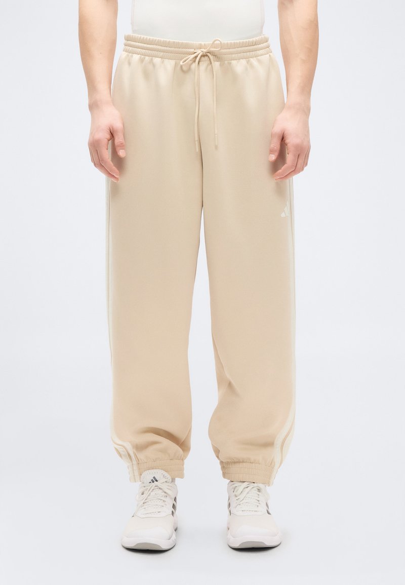 Beige sweatpants with a drawstring waistband, tapered cuffs, and white side stripes. Made of soft fabric, designed for comfort and ease.