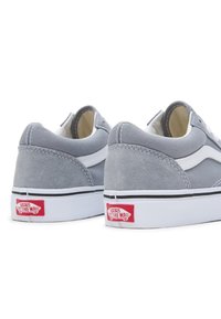 Zapatillas bajas de ante gris con acentos blancos, ribete negro y un logo rojo en el talón, que presentan un diseño clásico de zapatillas de skate.