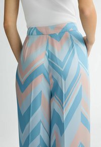 Leichte, pastellblaue Hose mit einem Chevron-Muster in Beige und dunklerem Blau. Geschmeidige Textur mit einem leicht lockeren Schnitt.