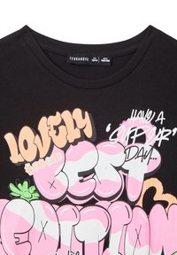 T-shirt in cotone nero con una stampa grafica colorata che include elementi testuali in rosa e bianco, tra cui la dicitura "Lovely" e dettagli come "#Fan Club!".