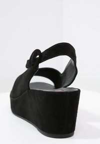 Černá semišová sandála na klínku s kulatou sponou a zvýšenou platformou. Hladký povrch na stélce; texturovaný vnější povrch.