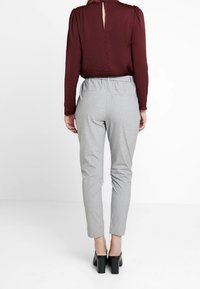 Blouse bordeaux avec détail en forme de clé à l'arrière, assortie à un pantalon tapered gris clair. Les pantalons possèdent une taille élastique, une texture lisse et sans motifs.