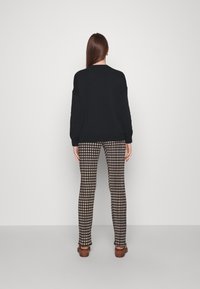 Svart stickad tröja med sänkt axel i kombination med rutiga, figurnära byxor i beige och svart. Modell som bär bruna klacksandaler.