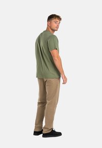 Olive green cotton t-shirt with short sleeves, relaxed fit. Paired with tan pants and black shoes, showcasing a casual, understated look.