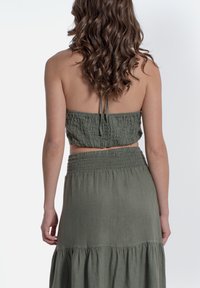 Completo a due pezzi verde oliva composto da un top corto smock e una gonna maxi a strati con cintura elastica. Tessuto leggero e testurizzato.