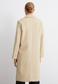 Beiger Wollmantel mit geradem Schnitt, Reverskragen, nahtlosem Rücken und langen Ärmeln. Glatte Textur mit minimaler Details.