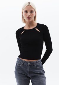 Top corto a maniche lunghe a coste nere con dettagli cut-out sul collo. Abbinato a jeans grigi chiari a vita alta con tasche davanti.