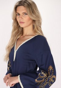 Rochie bleumarin cu decolteu în V, ornamentată cu broderie de nuanță aurie pe mâneci și dantelă albă în jurul gâtului.