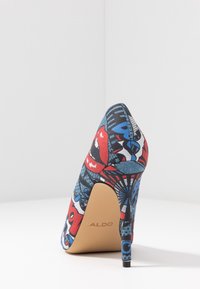 Chaussure à talons hauts avec un imprimé graphique coloré comprenant des motifs rouges, bleus et noirs. La semelle est beige avec le logo "ALDO". Tissu texturé.