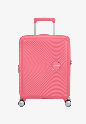 Valigia rigida rosa con design a onde concentriche, manico telescopico e quattro ruote piroettanti. Presenta un logo del marchio sul davanti.