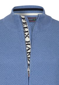 Ljusblå zip-up tröja med ett strukturerat mönster, kontrasterande navy- och vitrandig krage, samt en dragkedja med en logotyp som dragflik.