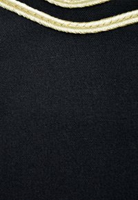 Czarna tkanina o teksturowanym wykończeniu, z dwoma złotymi plecionkami w pobliżu góry dla dodatkowego detalu.