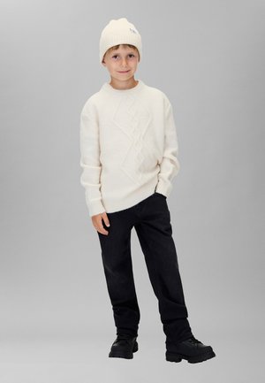 Cremefarvet strikket sweater med tekstureret diamantmønster, kombineret med mørke jeans og sorte snørestøvler. En ulden hue sidder på hovedet.