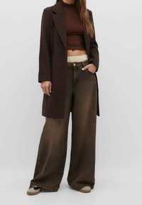 Bruine oversized jas met klapvallen, gecombineerd met een bruine crop top en brede bruine jeans met een lichte tailleband.