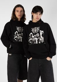 Zwarte hoodie met een witte grafische print van een gebouw, met een relaxte pasvorm en geribde manchetten. Gecombineerd met zwarte denim shorts.