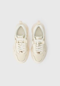 White chunky sneakers with textured soft material, lacing system, gold accent detail, and padded collar for comfort.