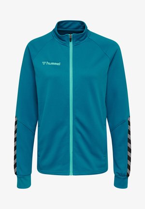 Teal zip-up jack gemaakt van textuurstof. Heeft een hoge kraag, contrasterende rits en zwart-grijze chevronaccenten op de mouwen.