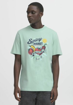 T-shirt od pamučne tkanine u mint zelenoj boji s grafičkim printom koji prikazuje papriku i sunce. Kratki rukavi, okrugli izrez, opušteni kroj i mekana tekstura.