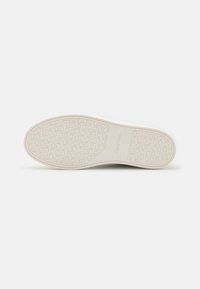 Semelle de chaussure présentant un design texturé avec une traction à motif, de couleur beige clair, et un logo embossé "Calvin Klein".