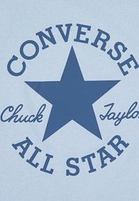 Šviesiai mėlynas audinys su dideliu tamsiai mėlynu žvaigždės raštu. Tekstas skelbia "CONVERSE" virš žvaigždės, "Chuck Taylor" žemiau ir "ALL STAR" aiškiai išryškintas.