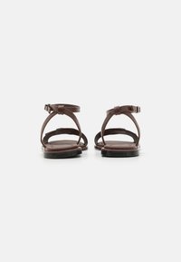 Brune lærsandaler med flad sål og ankelremme. Har et åbent tådesign og en minimalistisk spænde detalje.