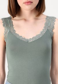 Green tank top with a V-neck design. Features delicate lace trim on the shoulders and a smooth, stretchy fabric texture.